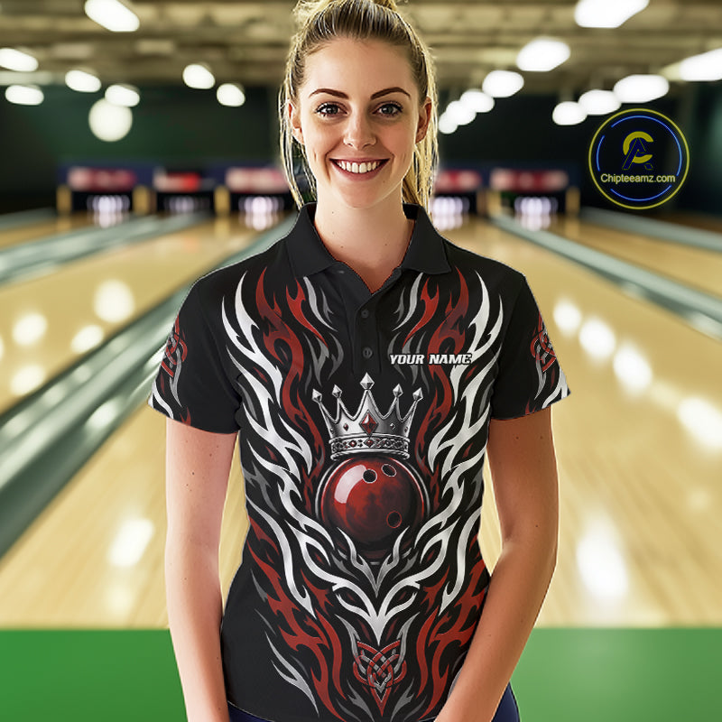 A woman wearing a black short-sleeve bowling-themed polo shirt with a red and white flame design, a crown, and a bowling ball graphic, standing in front of a blurred bowling alley background. 