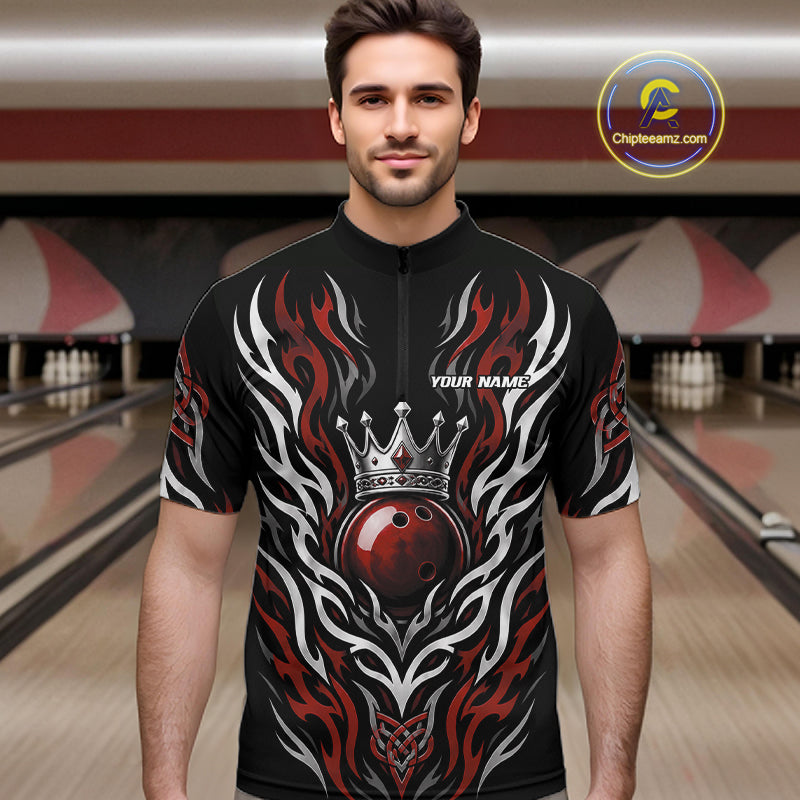 A man wearing a black short-sleeve quarter zip shirt bowling jersey with a red, white, and gray flame and crowned bowlinh ball graphic design, standing in a bowling alley. 