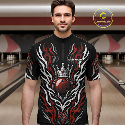 A man wearing a black short-sleeve quarter zip shirt bowling jersey with a red, white, and gray flame and crowned bowlinh ball graphic design, standing in a bowling alley. 