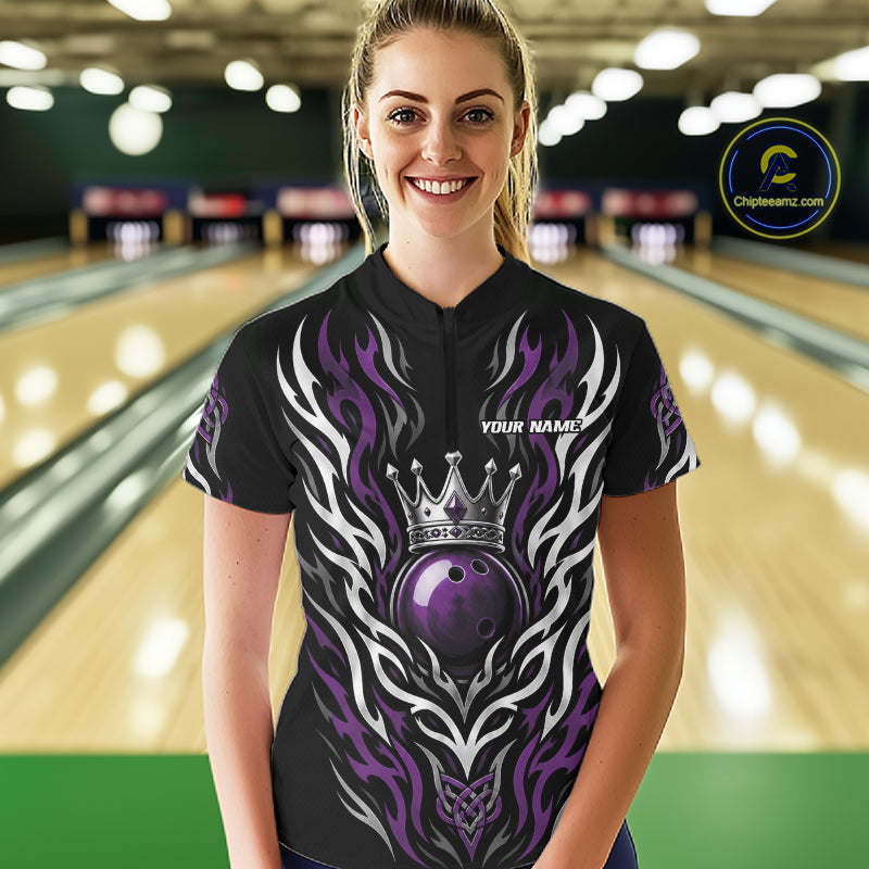 A woman stands in a bowling alley wearing a black short-sleeve quarter zip shirt with a purple and white flame design, a large purple bowling ball with a silver crown, and 'YOUR NAME' printed on the chest. 