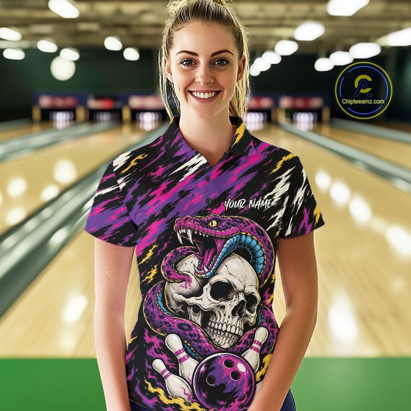 A woman stands in a bowling alley wearing a short-sleeve bowling polo shirt with a bold graphic print featuring a skull, snake, bowling pins, and bowling ball on a black, purple, and pink patterned background.