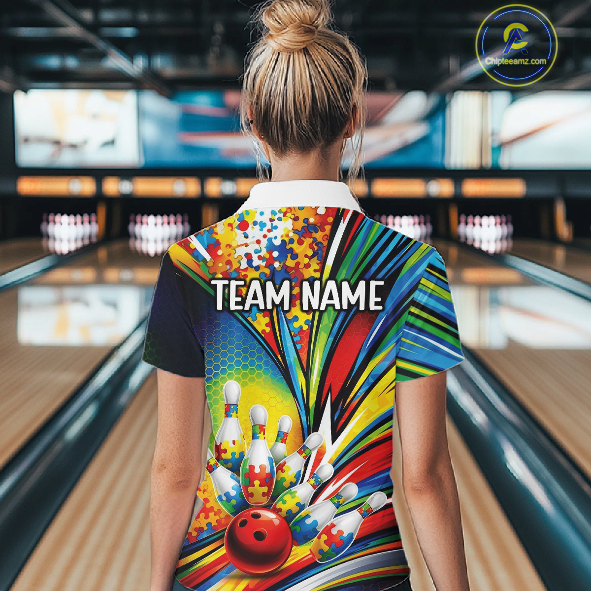 Back view of a female bowler wearing a quarter-zip shirt, colorful autism-themed bowling artwork with puzzle-inspired visuals.