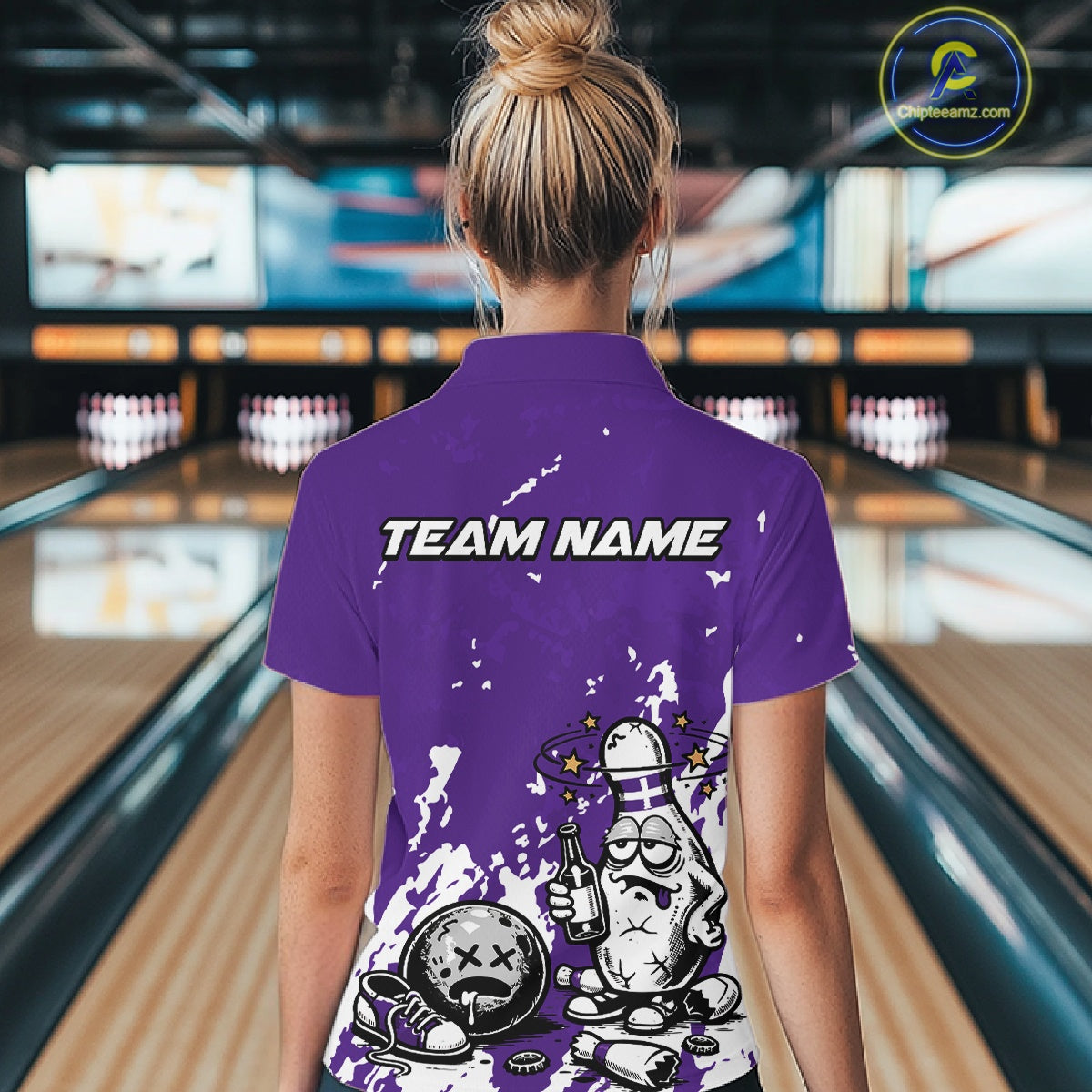 Back view of a female bowler wearing a purple and white polo shirt, splatter-style humorous bowling pin artwork holding beer bottle and bowling ball.