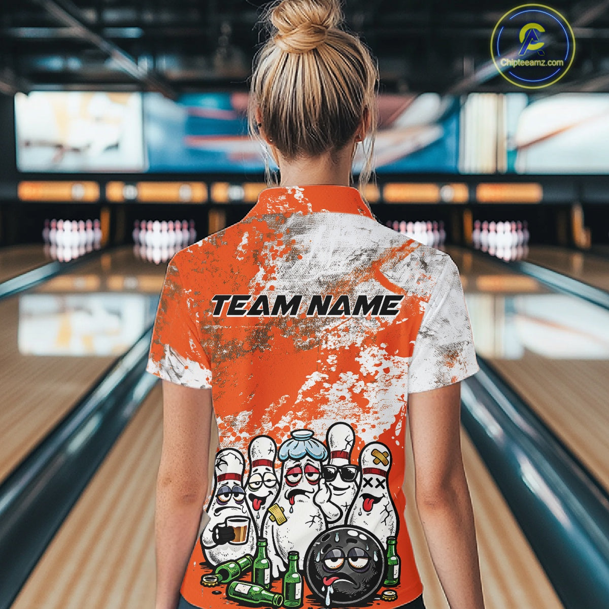 Back view of a female model in a bowling lane wearing an orange and white grunge splatter bowling quarter-zip shirt featuring cartoon bowling pins and bowling ball illustration.