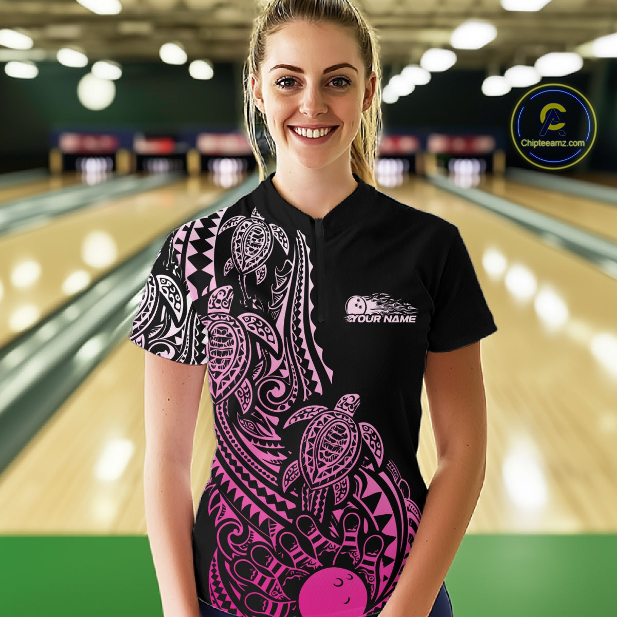Female model wearing a black and pink bowling quarter-zip shirt at the lane with turtle Polynesian patterns and bowling-themed graphics.