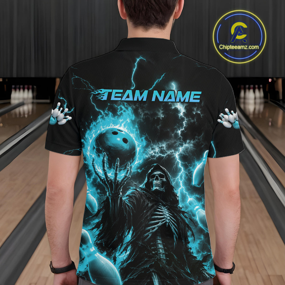 A man viewed from behind wearing a black short-sleeve bowling shirt with a large blue and black graphic of a skeletal figure, lightning, and a bowling ball. The shirt has 'TEAM NAME' printed across the upper back, and the man is standing in a bowling alley.