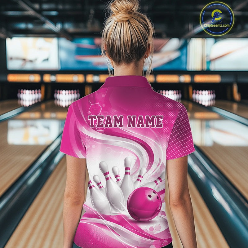 Back view of a female model wearing a white and pink bowling quarter-zip shirt in a bowling alley featuring flowing abstract wave patterns and a glossy bowling ball striking a set of pins