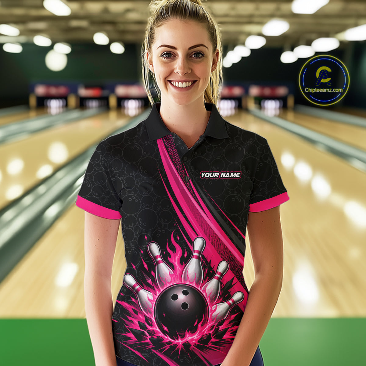 A woman wearing a custom bowling-themed polo shirt with a black and pink flame bowling ball graphic, standing in a bowling alley. 