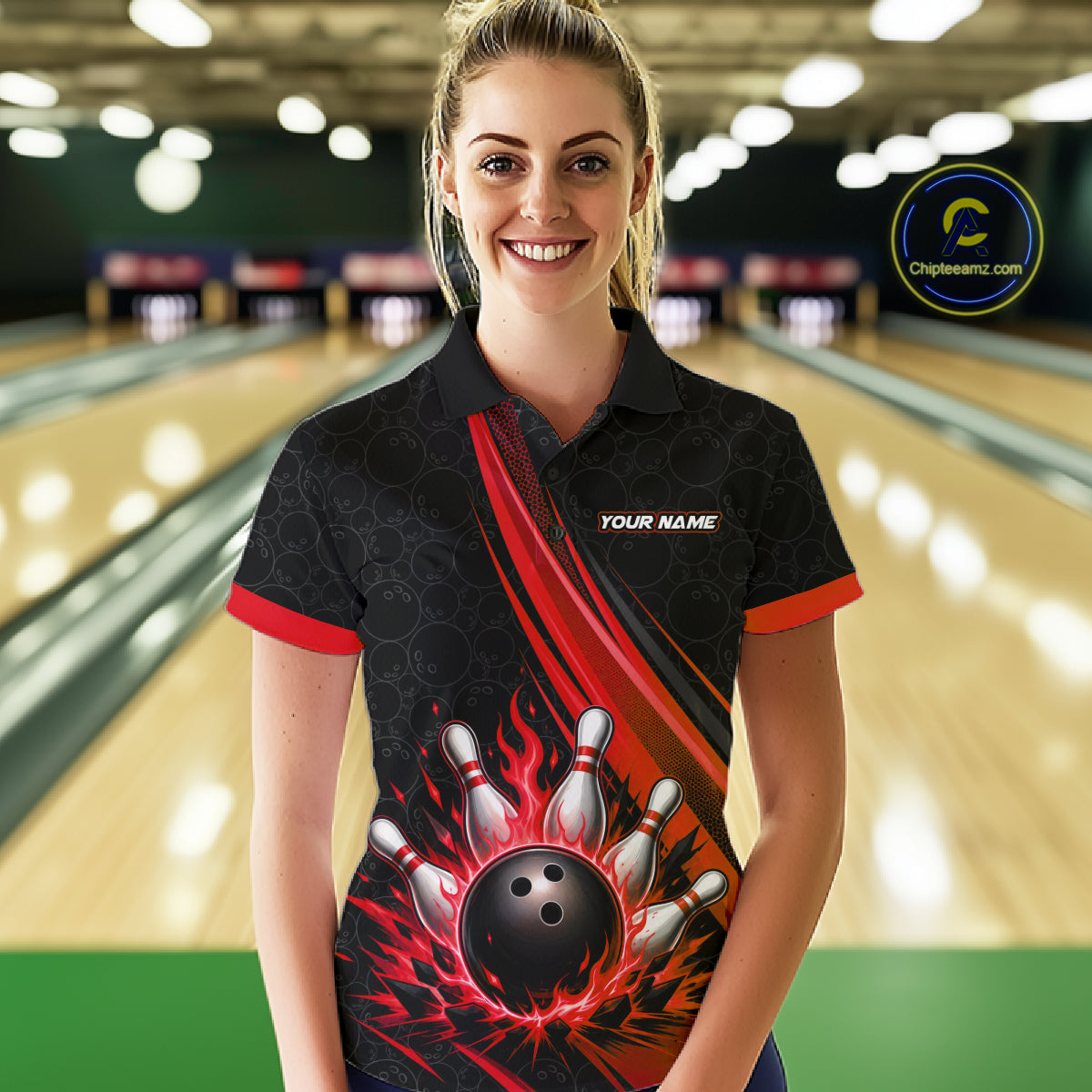 A woman stands in a bowling alley wearing a black short-sleeve polo shirt with a red and black bowling-themed graphic on the front, including bowling pins, a bowling ball, flames, and the text 'YOUR NAME'.