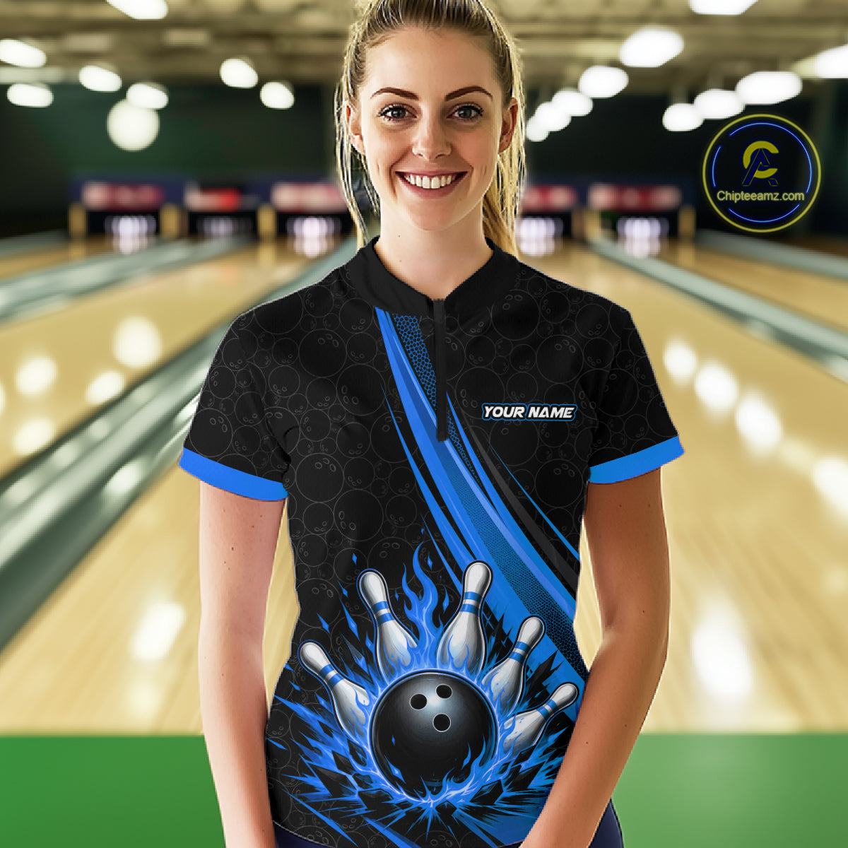 A woman stands in a bowling alley wearing a black short-sleeve bowling quarter zip shirt with blue flame-like graphics, bowling pins, and a bowling ball design on the front, along with 'YOUR NAME' text on the chest. 