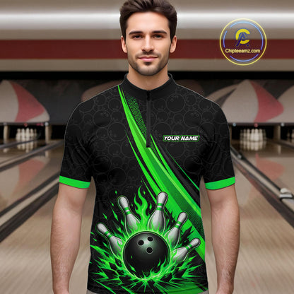 A man wearing a black short-sleeve bowling-themed quarter-zip shirt with bright green flame and pin graphics, standing in a bowling alley. 