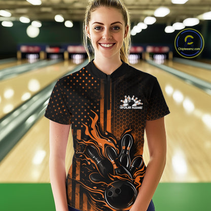 Female model at a bowling lane wearing a black and orange bowling quarter-zip shirt with fiery bowling strike graphics and flag-inspired styling.