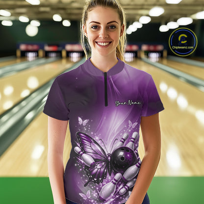 Female model at a bowling lane wearing a purple quarter-zip bowling shirt with butterfly artwork, a bowling ball, and scattered pin graphics.