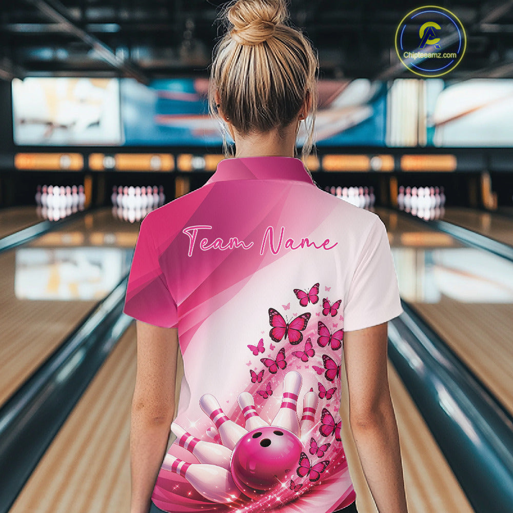 Back view of a female model wearing a white and pink bowling polo with butterfly graphics and bowling artwork at the bowling lane