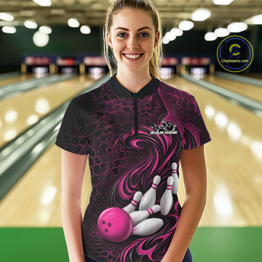 Female model standing in a bowling lane wearing a black and pink bowling quarter-zip shirt featuring a tribal flame bowling ball and pins graphic on the front.