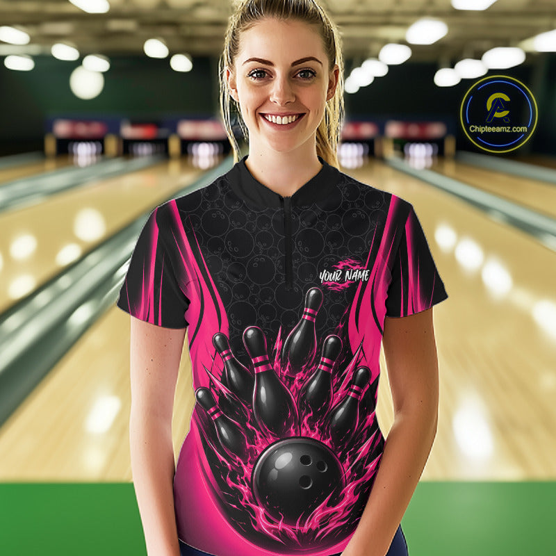 A woman stands in a bowling alley wearing a custom bowling jersey with a black and hot pink flame design featuring bowling pins and a ball graphic. 
