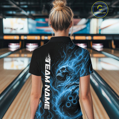 Back view of a female model wearing a black bowling polo shirt in a bowling alley featuring a skull clutching a bowling ball surrounded by swirling blue energy flames