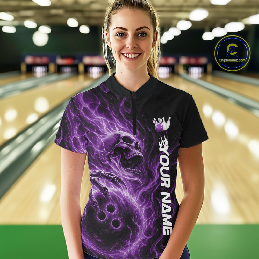 Female model wearing a black bowling quarter-zip shirt in a bowling alley featuring a skull clutching a bowling ball surrounded by swirling purple energy flames