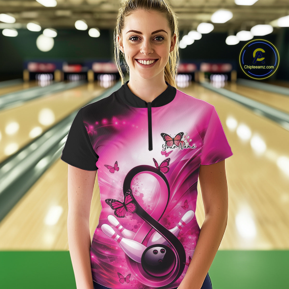 Female model at a bowling alley wearing a quarter-zip shirt featuring pink awareness and bowling-inspired artwork.