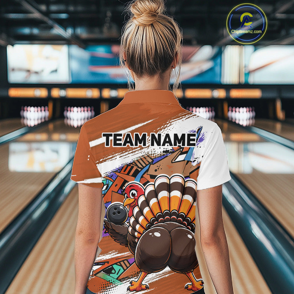 Back view of a female model wearing an orange custom bowling polo shirt with a funny graffiti turkey holding a bowling ball, paint splatter accents, and a personalized name in a bowling alley.