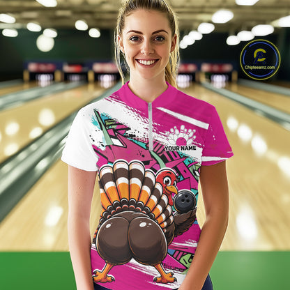 Front view of a happy female model in a bowling alley wearing a pink custom quarter zip bowling shirt with a funny graffiti turkey holding a bowling ball, paint splatter accents, and a personalized name.