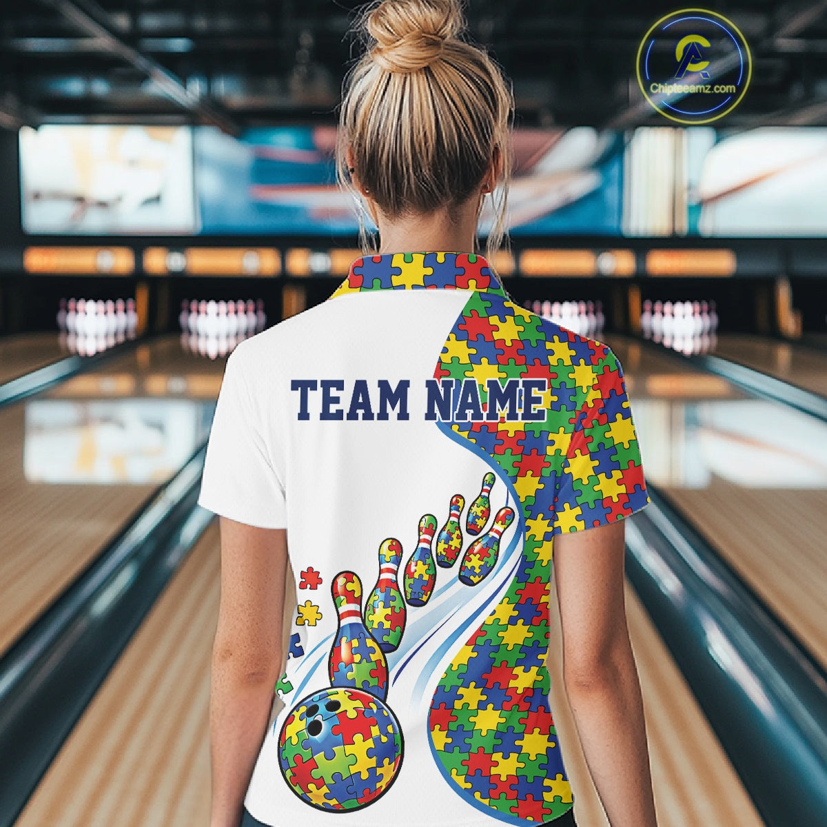 Female model in a bowling lane wearing a white polo shirt, back view featuring colorful autism-themed bowling strikes and puzzle-inspired graphics