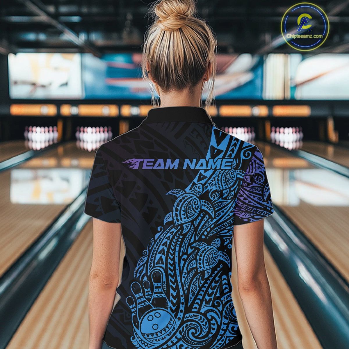 Back view of a female model in a black, blue, and purple bowling quarter-zip shirt showcasing turtle-themed tribal bowling artwork.