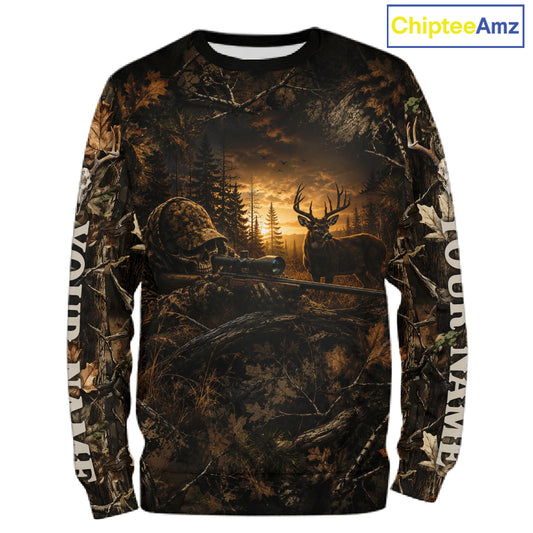 A long-sleeve crewneck shirt featuring an all-over camouflage and hunting-themed graphic print. The design depicts a deer hunter in camouflage with a rifle, a deer with large antlers, a forest silhouette, and a glowing sunset.