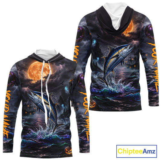 A long-sleeve hooded sweatshirt shown from the front and back, featuring an all-over Halloween-themed graphic print with a jumping blue tuna fish, dark stormy sky, orange full moon, and glowing orange text on the sleeves. The hoodie has a black hood with white drawstrings and a white inner collar.