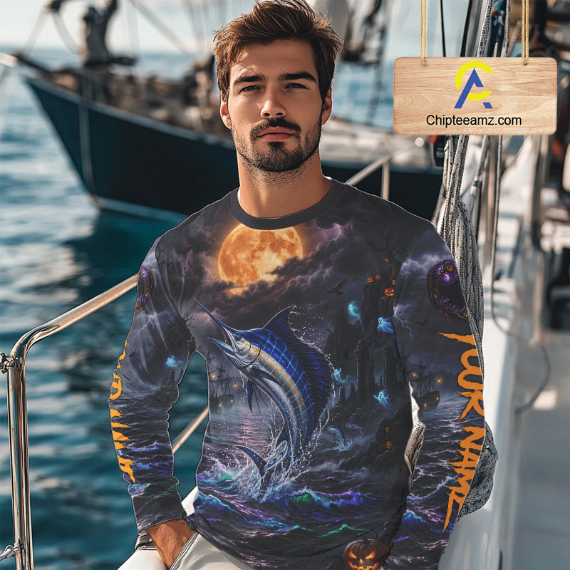 A man wearing a long-sleeve crewneck shirt with an all-over Halloween-themed graphic print featuring a marlin, a full moon, and orange vertical text on the sleeves, photographed on a boat deck with a visible Chipleeamz.com watermark overlay.