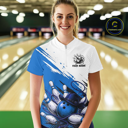 A woman stands in a bowling alley wearing a custom short-sleeve bowling jersey. The jersey is white on the upper chest and shoulders, featuring a blue brushstroke design that transitions into a graphic of bowling pins and bowling balls.