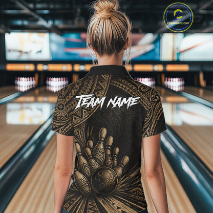 A woman viewed from behind wearing a black short-sleeve bowling-themed polo shirt with a large gold hand graphic and the words 'TEAM NAME' across the back, standing in a bowling alley.