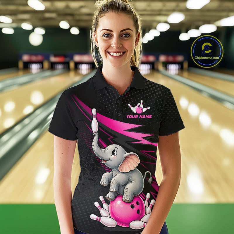 A woman wearing a black bowling-themed polo shirt with a cartoon elephant and pink bowling ball graphic, standing in a bowling alley. The shirt features a pink lightning bolt, a gray cartoon elephant on a pink bowling ball, and white bowling pins.