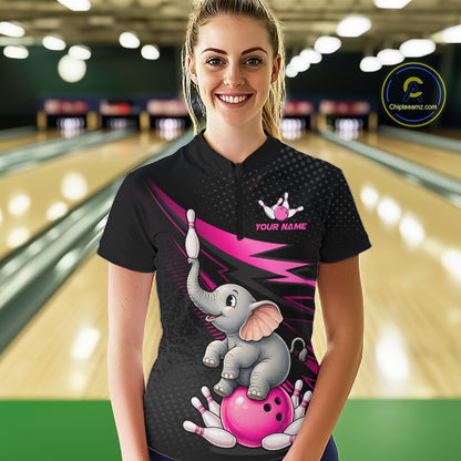 A woman stands in a bowling alley wearing a black short-sleeve bowling shirt with a colorful cartoon elephant and pink bowling ball graphic. The shirt has a small crown logo and the text 'YOUR NAME' on the chest.