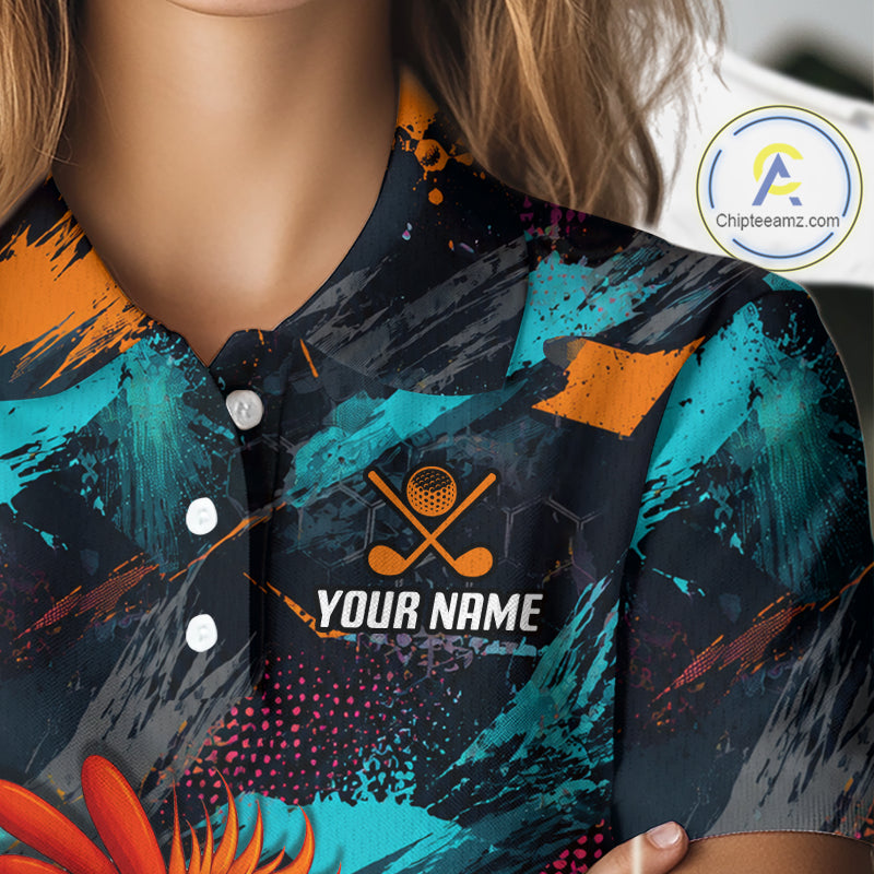 A close-up of a person wearing a short-sleeve collared polo shirt with a dark abstract paint-splatter design in teal, orange, and black, featuring crossed golf clubs and the text 'YOUR NAME' on the chest.