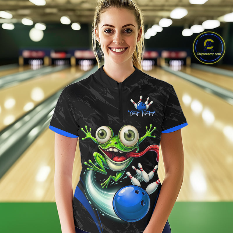 A woman stands in a bowling alley wearing a black short-sleeve bowling jersey with a colorful cartoon frog graphic, blue trim, and a blue bowling ball illustration. The background shows blurred bowling lanes, and a circular 'Chipteeamz"