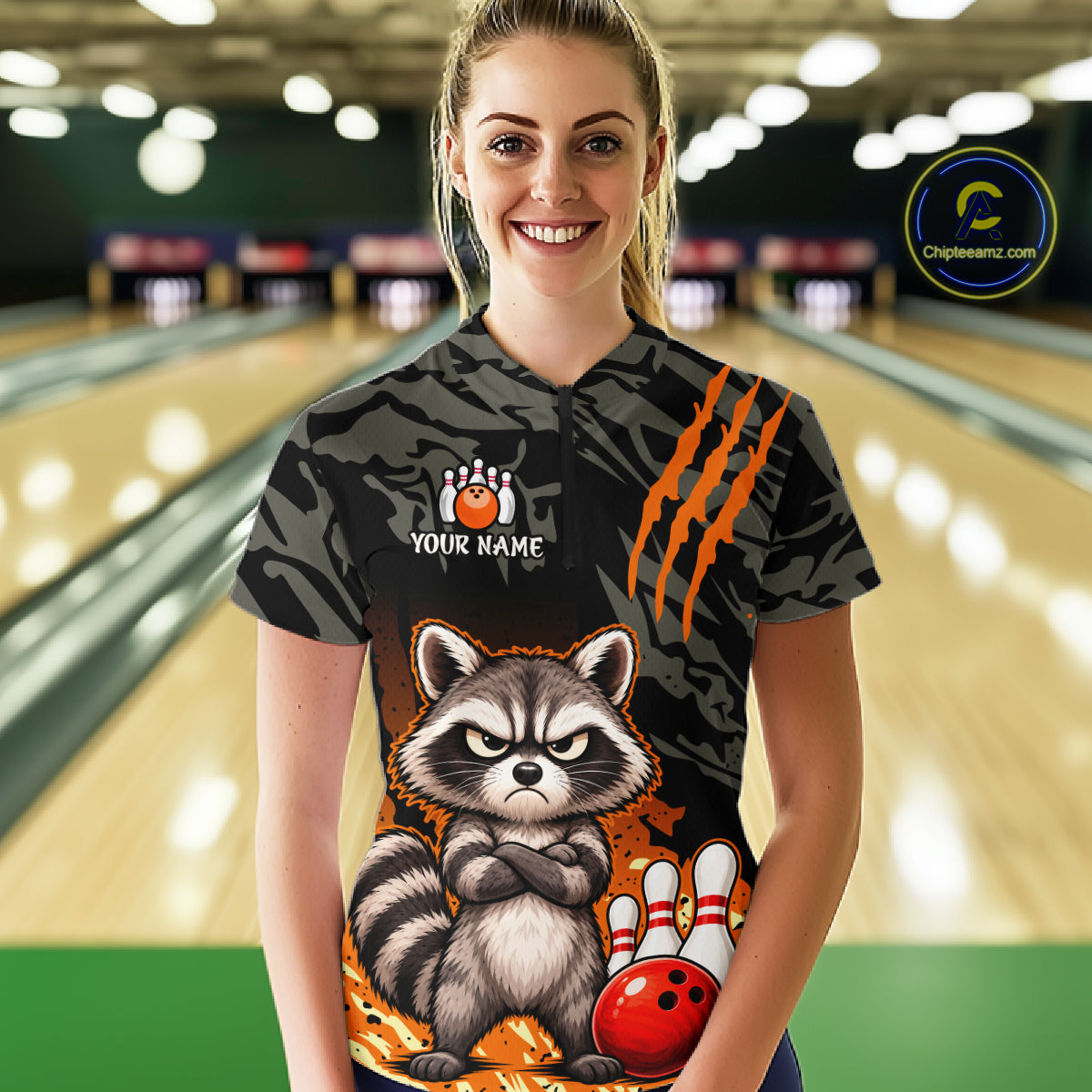 A woman stands in a bowling alley wearing a custom short-sleeve bowling t-shirt with a raccoon graphic, claw marks, and a bowling pin logo. The background shows blurred bowling lanes.