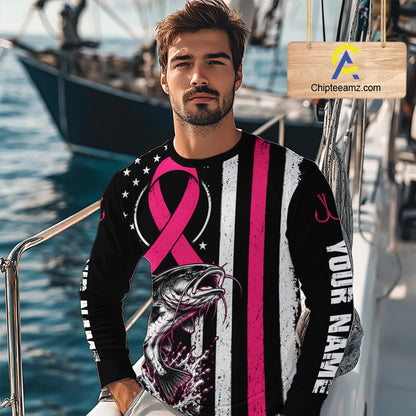 A man wearing a long-sleeve graphic shirt with a pink ribbon, a fish design, and vertical black, white, and pink stripes, standing on a boat with water and another boat in the background. A wooden sign with the text 'Chipleeamz.