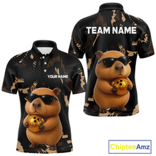 Load image into Gallery viewer, Black polo shirt with a capybara holding a gold ball design, customizable text, and Chiptee Amz branding.