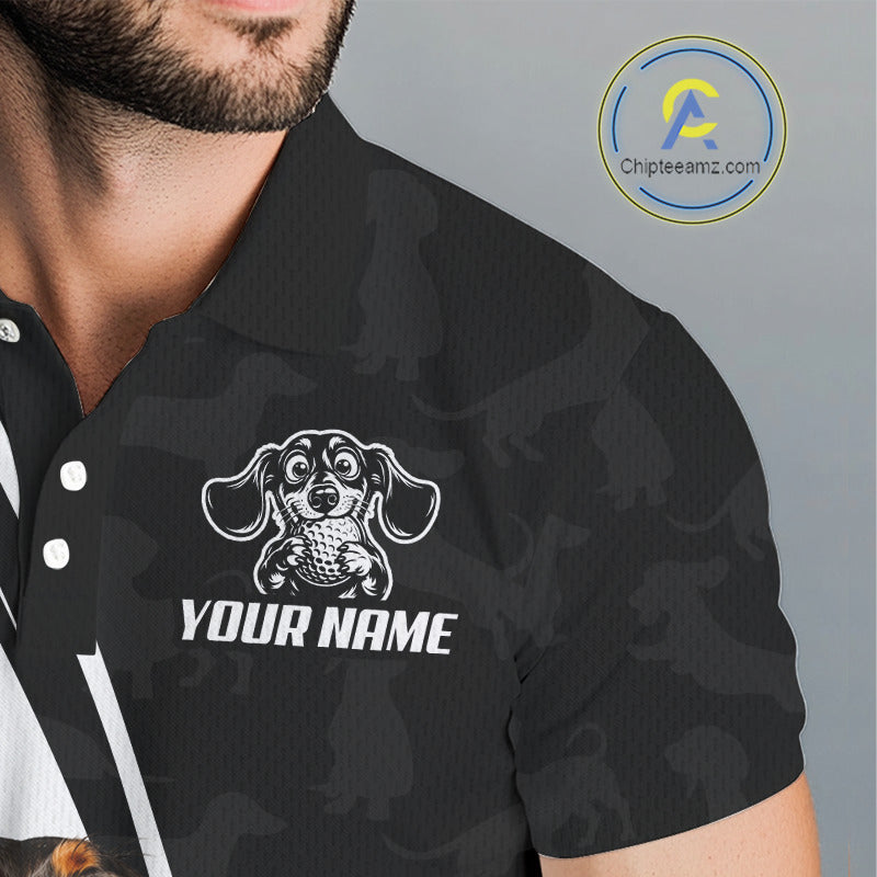 A close-up of a man wearing a black short-sleeve polo shirt with a dark gray camouflage pattern. The shirt features a white graphic of a dachshund dog and the text 'YOUR NAME' on the chest, indicating a customizable product.