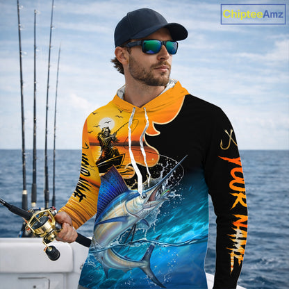 Man wearing a colorful long sleeve hooded fishing shirt with a design of a sailfish fish and a fish reaper, standing on a boat with fishing rods in the background.